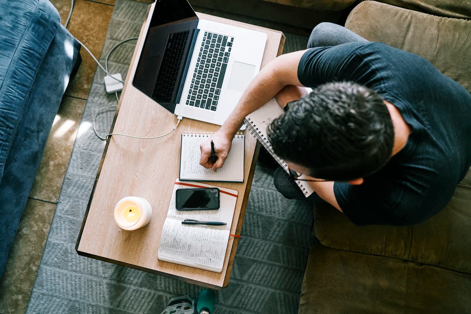 Someone taking notes at home beside a laptop